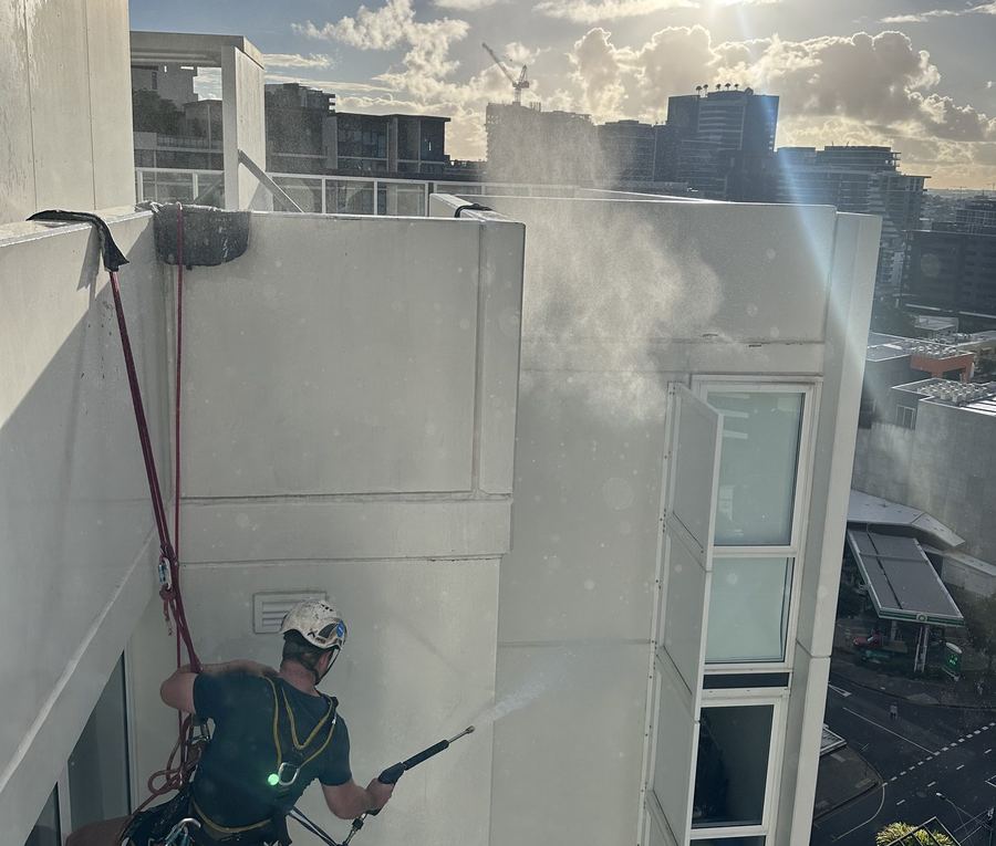 Rope access technician cleaning a building facade before coating